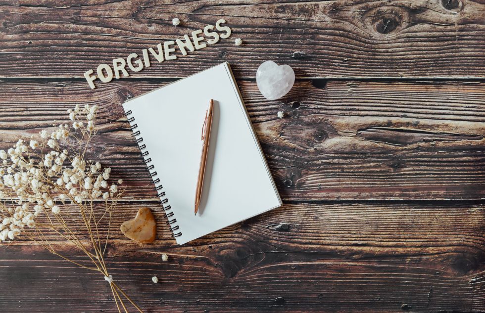 The Power of Forgiveness with a pen on a pad of paper on a wood table, with flowers.